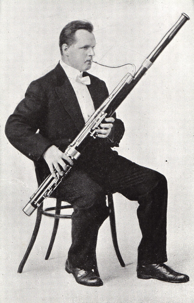 William Gruner sits in a chair, wearing a tuxedo, playing the bassoon